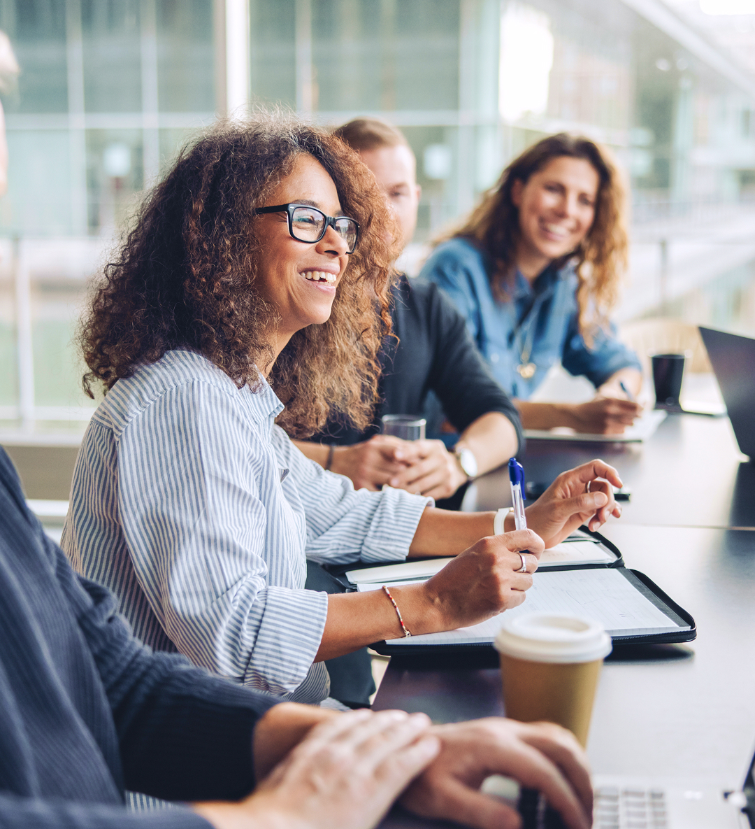 A woman presents in front of peers, sitting around a conference table